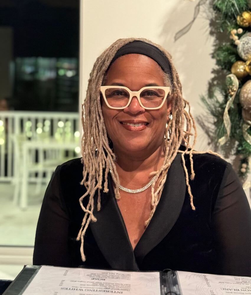 Black woman wearing glasses with white frames and black blouse sitting at table